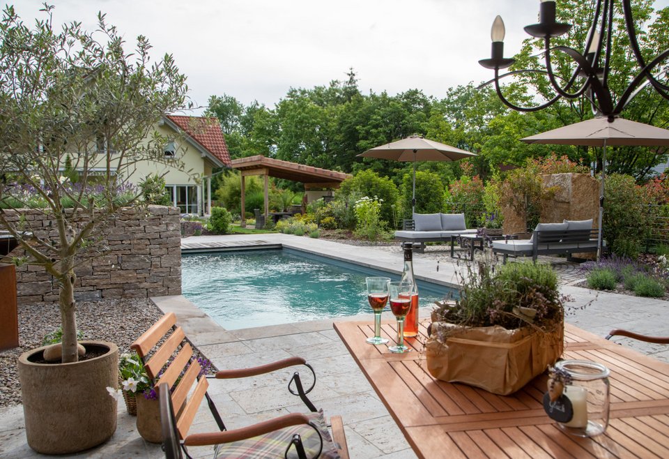 Innenhof mit TeichMeister Pool, umgeben von Gartenmöbeln wie Holzstühlen, Liegen und Tischen.