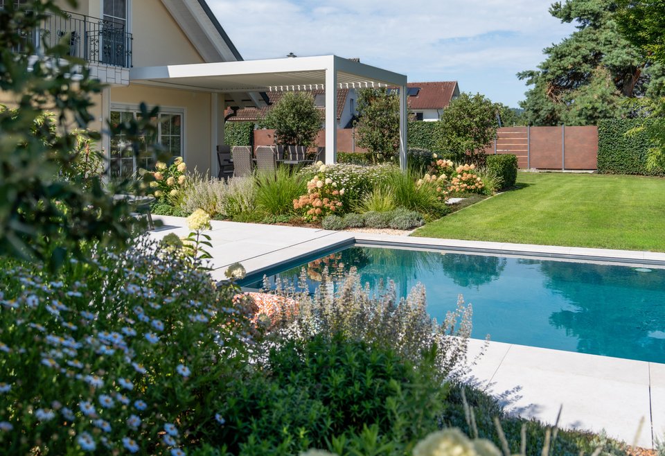 Garten mit Swimmingpool Moderner Garten mit klarem Swimmingpool, gepflegtem Rasen, blühenden Blumen und einer überdachten Terrasse neben einem Haus.