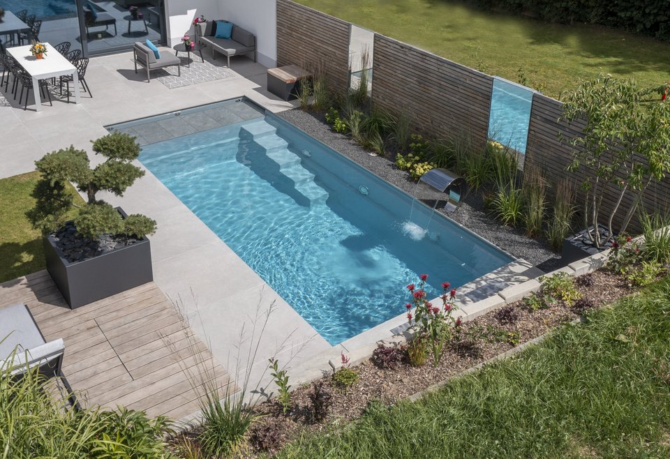 TeichMeister Swimmingpool im Garten mit klar blauem Wasser, Treppenstufen zum Einstieg, umgeben von Terrasse, Pflanzen und Gartenmöbeln.