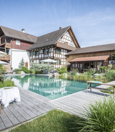 Ein traditionelles Fachwerkhaus mit angrenzendem modernen Neubau umgibt einen TeichMeister Naturpool.