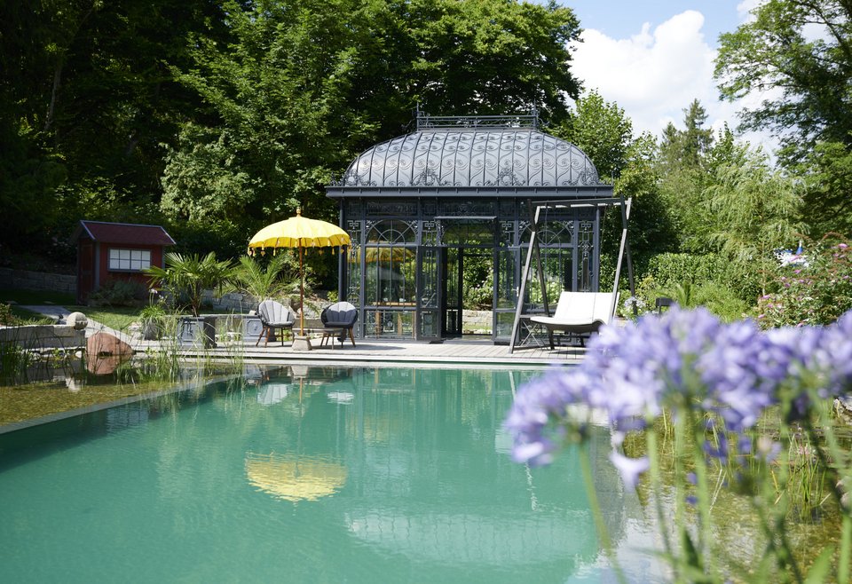 Ein gepflegter Garten mit einem großen Schwimmteich, davor blühende Blumen.